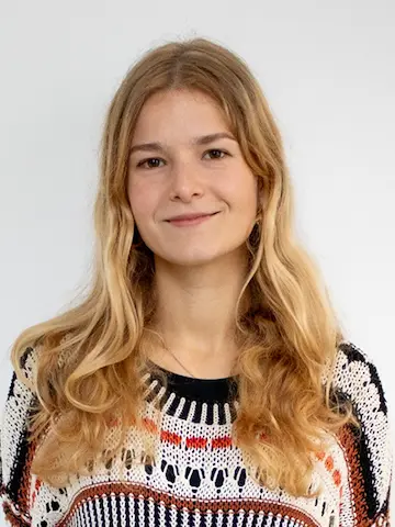 A woman with long fair hair wearing a kitted jumper against a pale background.