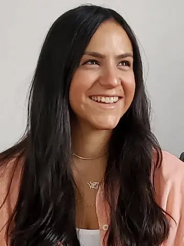 A smiling woman with long dark hair and a light top looking off to the side.
